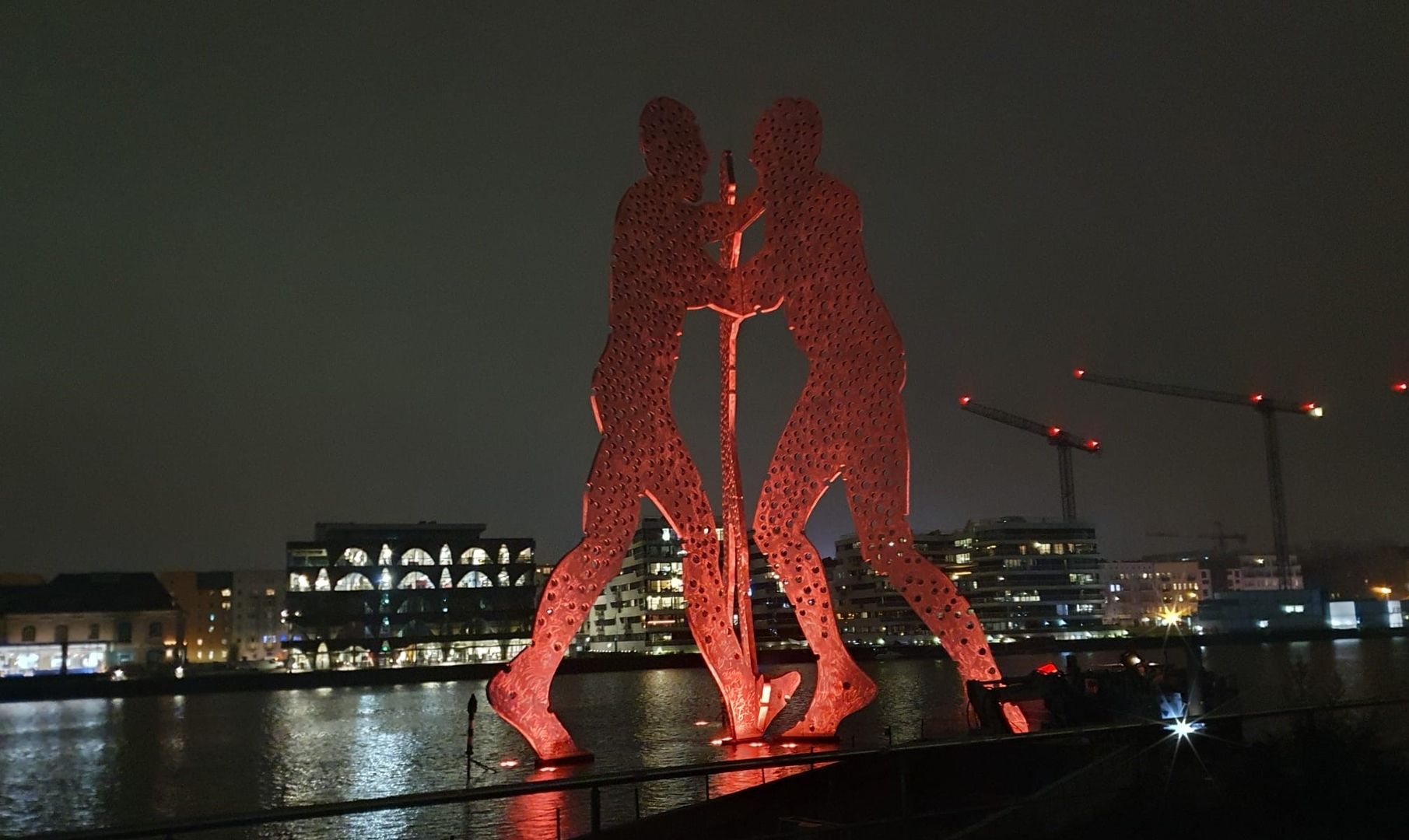 Rote Skulptur (Molecule Man) von zwei Personen, die aus dem Wasser ragen, in einer ruhigen Umgebung